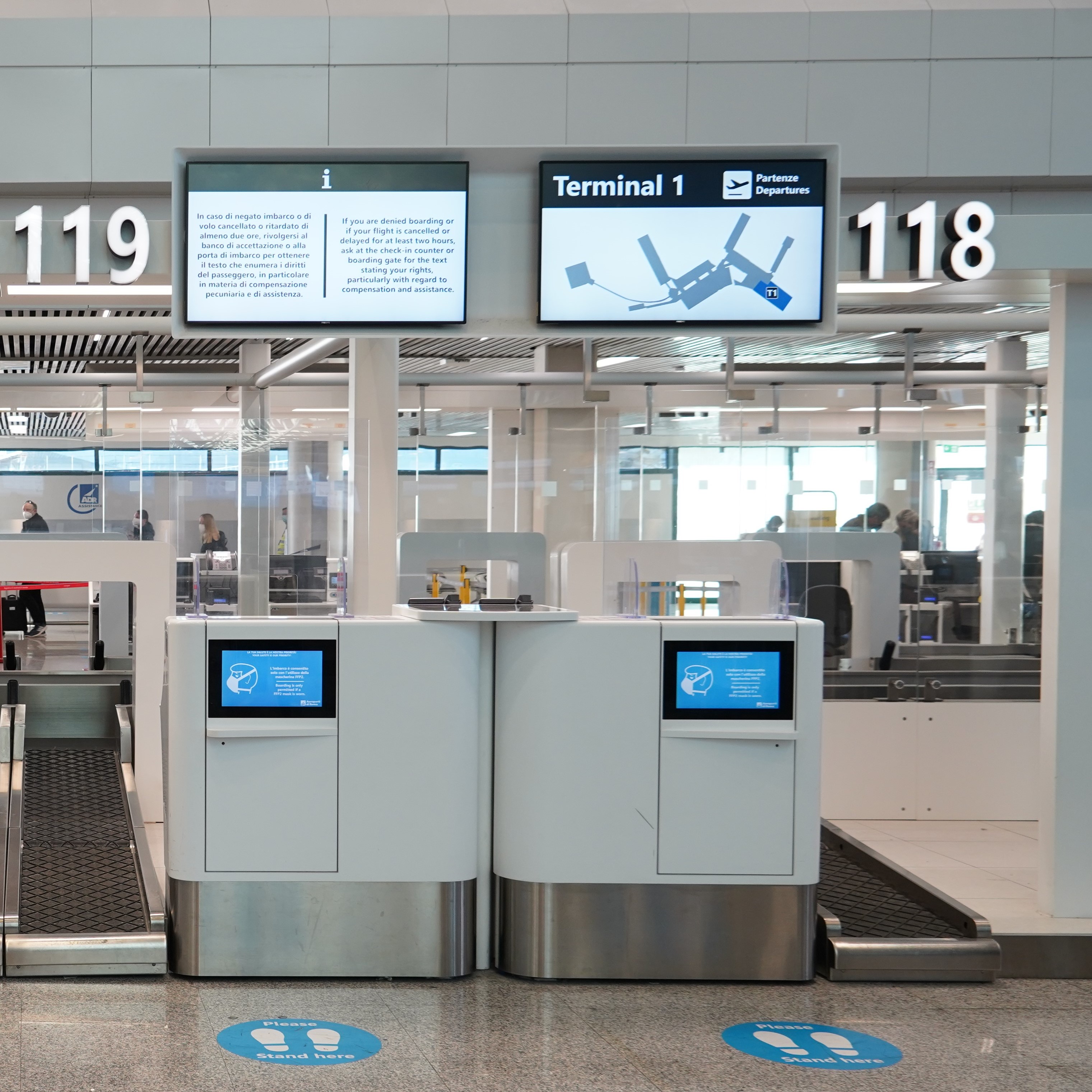 Area check-in dell’aeroporto con banchi self-service, indicazioni per le partenze del Terminal 1 e numeri dei banchi 118 e 119